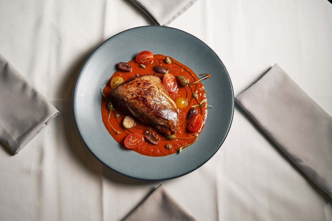 Poulet rôti sur lit de sauce tomate, olives et herbes
